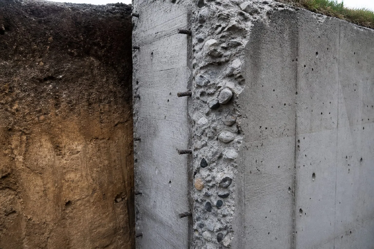 Mur de béton armé épais et terre tassée en coupe, montrant la masse qui sépare un local du dehors.